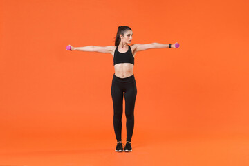 Fototapeta na wymiar Full length portrait of beautiful young fitness sporty woman in black sportswear posing training working out doing exercise with dumbbells looking aside isolated on orange color background studio.