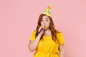Cheerful young redhead plus size body positive female woman girl 20s in yellow dress birthday hat...
