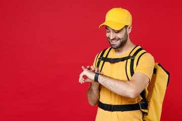 Delivery man in yellow cap t-shirt uniform thermal bag backpack with food hand smartwatch isolated on red background studio Guy male employee work as courier Service coronavirus covid-19 virus concept