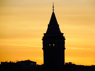 Silueta oscura de Torre Galata en Estambul (Turquia) al atardecer con cielo amarillento que destaca sobre los edificios del centro de la ciudad y parte superior cónica con un mirador y restaurante