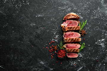 Grilled sliced beef steak with rosemary and spices on a black stone background. Top view. Free space for your text.