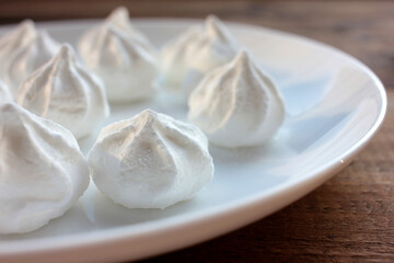 Fototapeta na wymiar Close-up of meringue on a white plate. Marshmallows on wooden table background