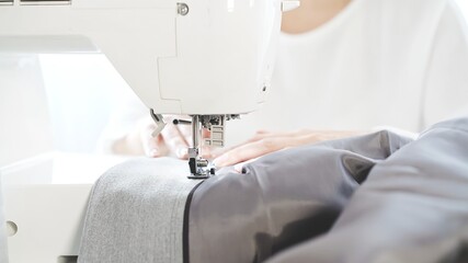 Female hands sew on a white sewing machine close-up. Concept of sewing courses, woman in white sweater sewing grey cloth in process