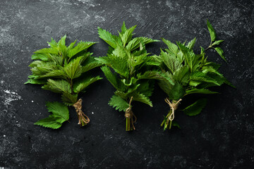 Fresh green nettles. Healthy herbs on a black stone background. Top view.