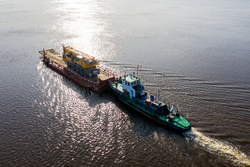 A tug pushes a barge loaded with a car crane. Shooting from a drone.