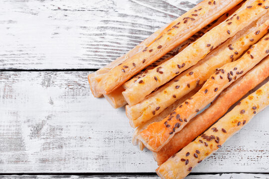 Breadsticks of puff pastry with flax seeds against the white wooden background