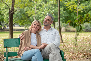 Happy Senior Caucasian couple hugging and holding hand together in while sitting at bench in the park.