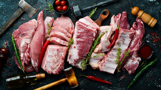 Set of raw meat. Pork meat on black stone background with spices and herbs. Top view. Rustic style.