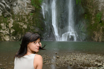 Beautiful young woman sitting in front of waterfall.