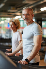 Portrait of mature muscle man looking at camera while training on treadmill in the gym