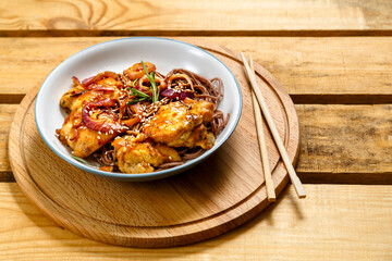 Plate of soba with chicken and sesame seeds in teriyaki sauce on a wooden stand and sticks.