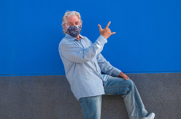 Cheerful senior man white hair wearing medical mask due to covid-19 smiles happy gesturing with...
