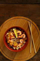 udon with mushrooms and shrimps in a clay plate on the table next to chopsticks.