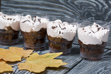 Zephyr in a glass. With biscuit and chocolate. Nearby are dried maple leaves. On pine boards painted black and white.