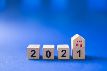 2021, Business, Mortgage, Home Loan Planning Concept. Closeup of mini wooden house toy on top of wooden number block  on blue background with copy space.