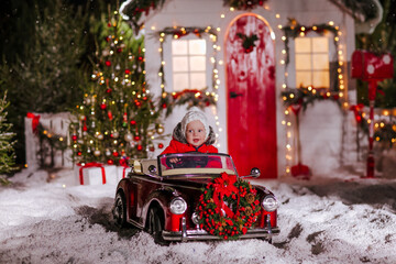 Fototapeta na wymiar lille boy sits in a red children's convertible in the snowy spruce forest