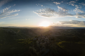Aerial view of stone town Civita di Bagnoregio with the sun at the sunrise with clay badlands and trees in background