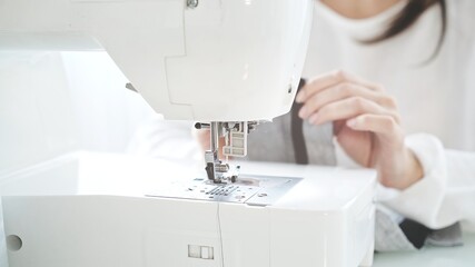 Concept of sewing courses in modern bright studio, sewing in process, blurred background. Female hands sew on a white sewing machine close-up. 