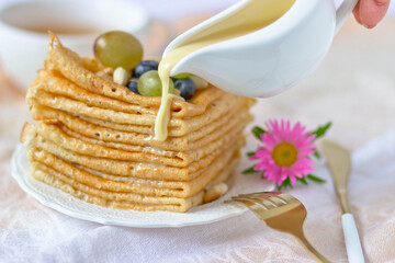 A stack of pancakes with grapes and peanuts poured with condensed milk on the background of a cup...
