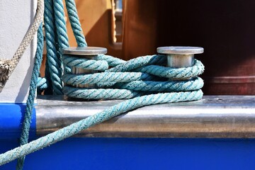 Fototapeta premium Chrome double bollard with blue mooring rope on the navy ship, close up.