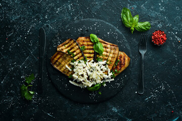 Food. Baked grilled eggplant with blue cheese and basil on a black stone plate. Top view. Free space for your text.