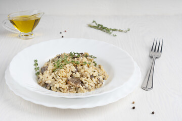 Traditional risotto or Italian arborio rice dish with broth, mushrooms, thyme, white wine and parmesan cheese served in plate with fork on white wooden background at kitchen. Image with copy space