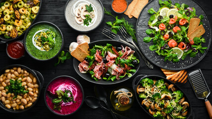 Background food and dishes. Salads, snacks and soups on black background. Top view.
