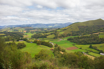Fototapeta na wymiar Scenic view of Pyrenees mountains with village in valley, France. Landscape of Camino de Santiago. Colorful meadows and farm in valley. Forest and farm on the hills. Panoramic view of mountains.