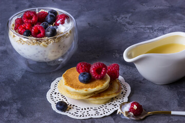 Rice flour pancakes and chia pudding with oatmeal, raspberries and blueberries, gravy boat with condensed milk on a gray background