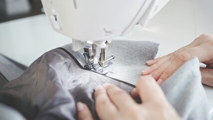 Concept of sewing in modern bright studio, woman in white sweater sewing grey cloth in process....