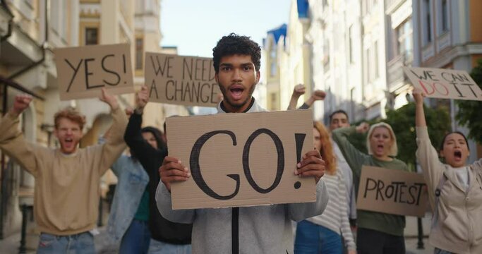 Mixed race man in front of demonstration shows Go poster to protest with activists in background.