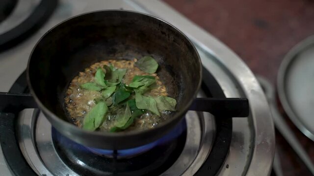 Adding Cardamon And Bay Leaves In A Small Deep Pan Over A High-Flamed Stove. - High Angle Shot