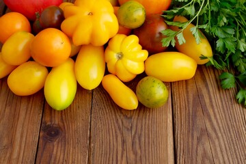 Various varieties of tomatoes and a bunch of green parsley on a wooden background.