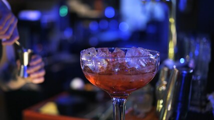 Red cocktail with ice on bar counter, background of night club dark light. Close up of glass with cocktail and ice, concept of cocktail making in night clubs, blurred background