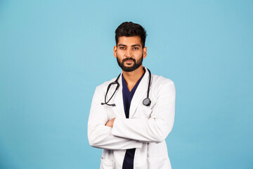 Fototapeta premium Handsome modern Indian / Asian doctor with stethoscope, in uniform on blue background