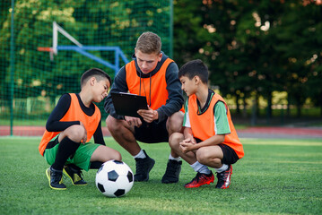 Professional soccer coach tells the strategy of football game to his attentive teen players at stadium during training.