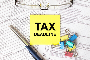 Yellow sticker with text Tax Deadline. Next to it is a blue pen with colored stationery clips and eyeglasses