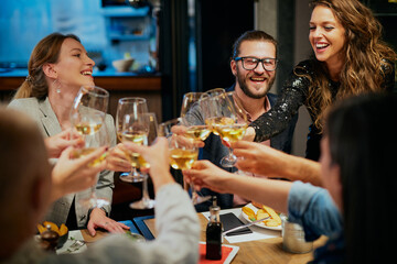 Group of friends celebrating in restaurant and toasting with white wine.