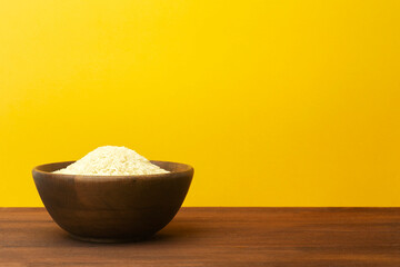 Wooden bowl with rice on a yellow colored background. Wooden plate with asian indian rice basmati on the table