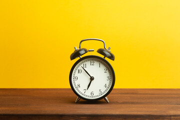 Vintage alarm clock on a yellow background. Black alarm clock showing morning time on the table....
