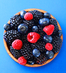 Bowl of fresh fruit. Blackberries,raspberries,blueberries on a bowl over blue background. Healthy breakfast. Vegan sweet food.