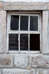 Altes verwittertes Fenster aus Holz in einer massiven Steinwand eines alten verlassenen Hauses