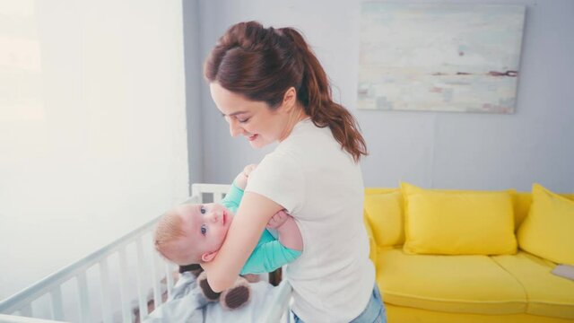 brunette mother holding in arms baby boy near crib 