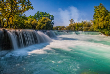 View of flowing Manavgat Waterfall in Antalya, Turkey, with green trees around, on cloudy blue sky...