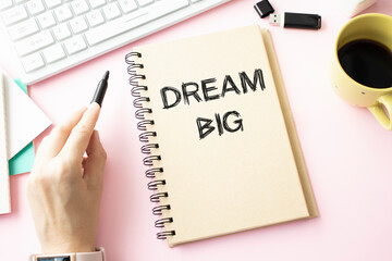 DREAM BIG on notebook on wooden desk with cup of coffee and pen