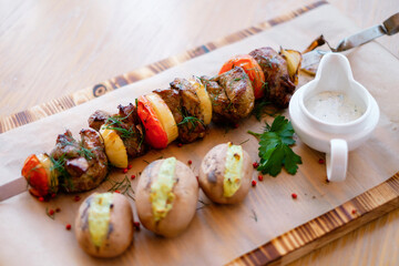 Fried  barbeque meat with vegetables on a skewer and potatoes. Grilled BBQ decorated with vegetables and sauce on wooden table and parchment paper.