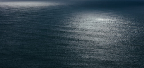 View of dappled sunlight on ocean waves and surf at dusk