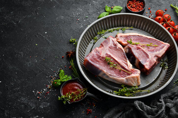 Dry raw two T-bone steak on the bone with spices on a black stone background. Top view. Rustic style.