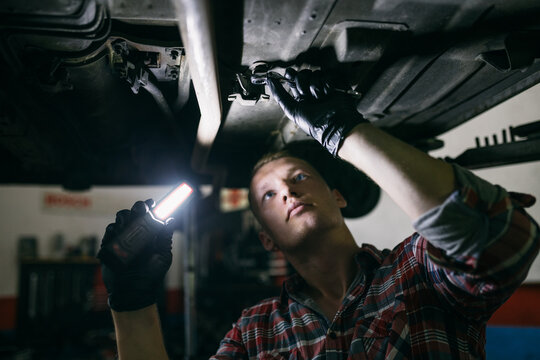 Repairman standing under car fixing it with light and tool