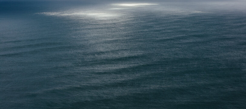 View of dappled sunlight on ocean waves and surf at dusk